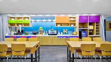 A modern restaurant with a blue wall, wooden tables and chairs, and a counter with various food items.