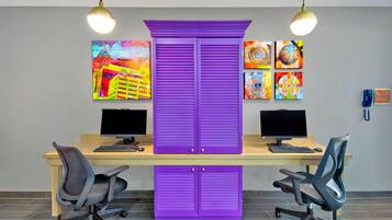 Ein Arbeitsbereich mit zwei Schreibtischen, jeweils ausgestattet mit einem Computer und einem Stuhl, sowie einem zentral platzierten violetten Schrank.