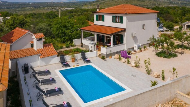 Una casa moderna de dos pisos con piscina, mobiliario exterior y vistas del paisaje circundante.