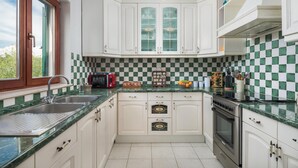 Una cocina con gabinetes blancos, salpicadero a cuadros, microondas, pileta y estufa.