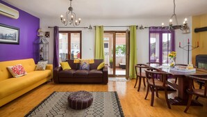 Una sala de estar con un sofá amarillo, un sofá marrón, un taburete estampado y un comedor con una mesa y sillas de madera.