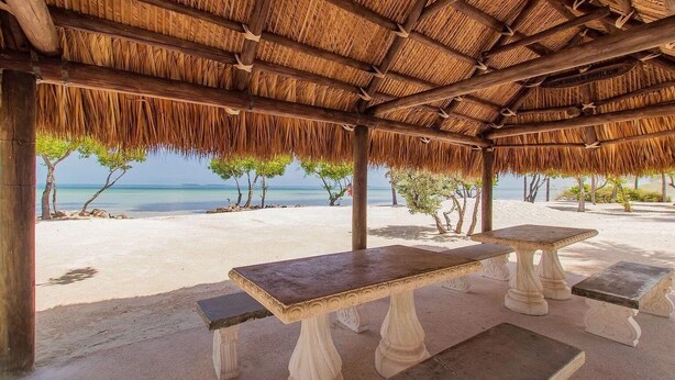 A beachside pavilion with a thatched roof, a table, and benches. - Island pool home awaits in Islamorada's Port Antigua (Islamorada)
