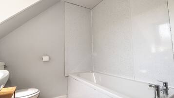 Et badeværelse med toilet, vask og badekar.