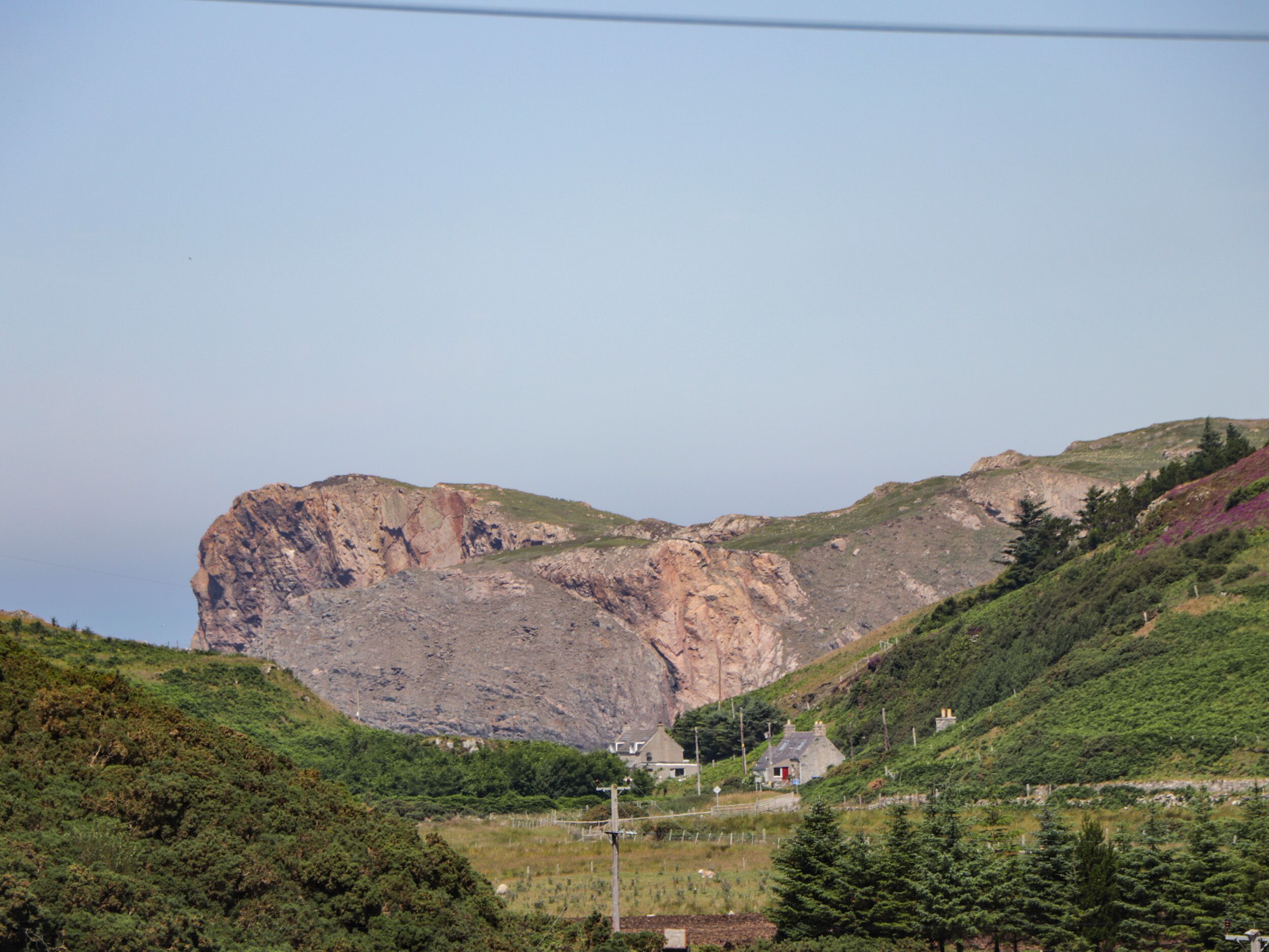 A mountainous landscape with a prominent rocky cliff and a small settlement with houses at the base.