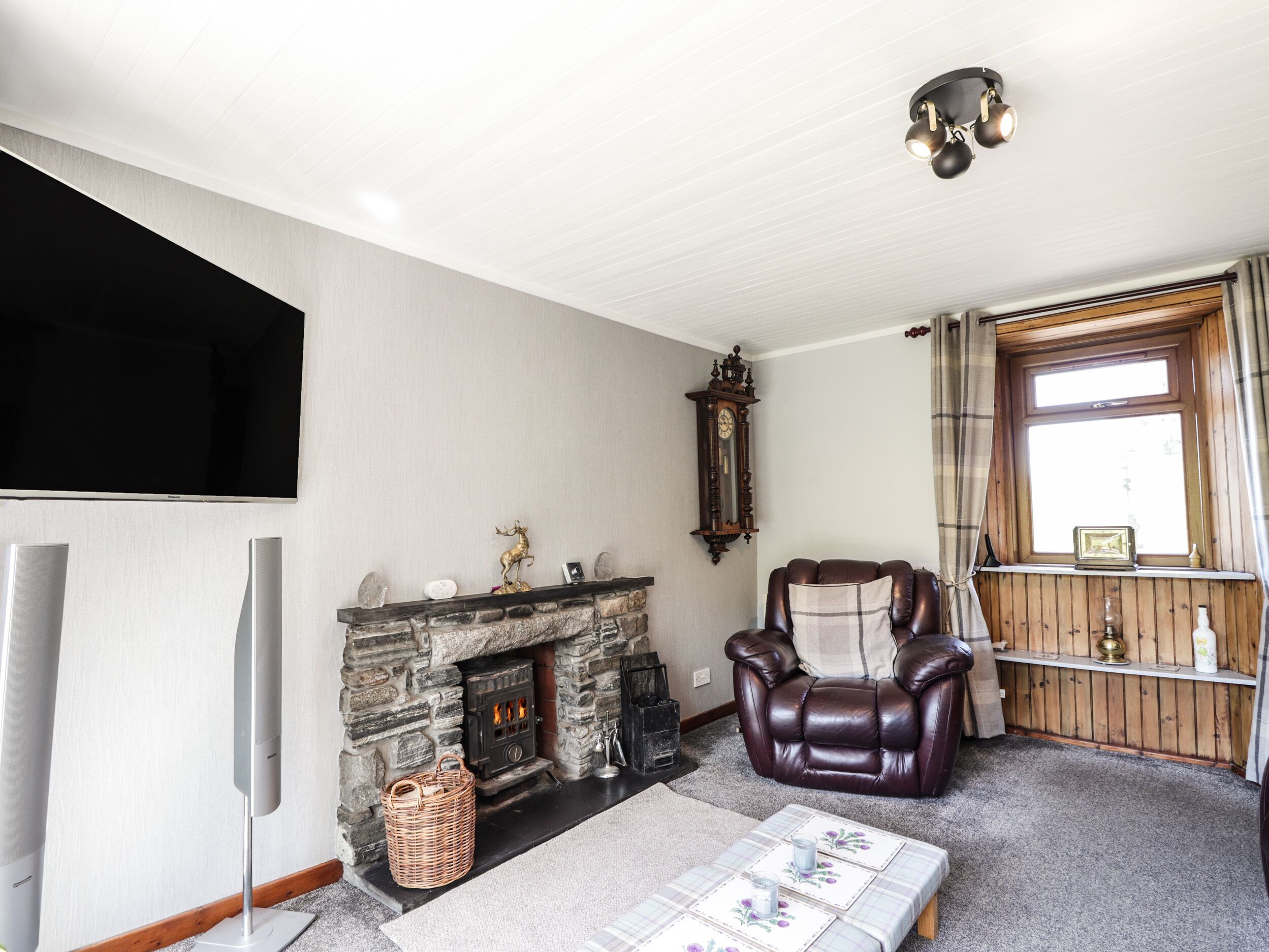 A living room with a stone fireplace, leather armchair, and a flat-screen TV.