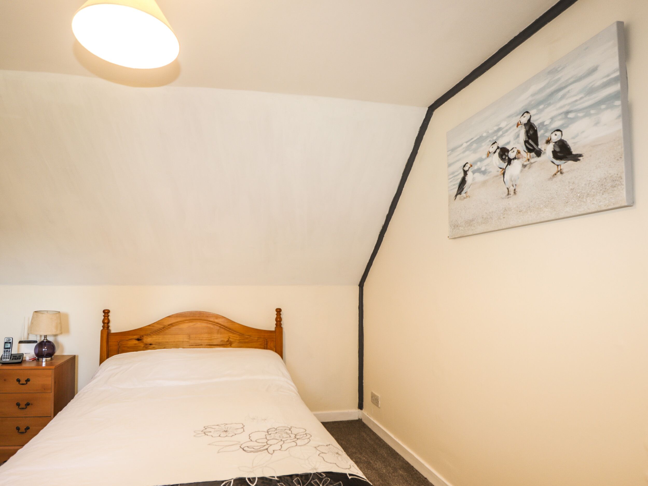 Une chambre à coucher avec un lit en bois, une table de chevet avec une lampe et un tableau représentant des oiseaux accroché au mur.