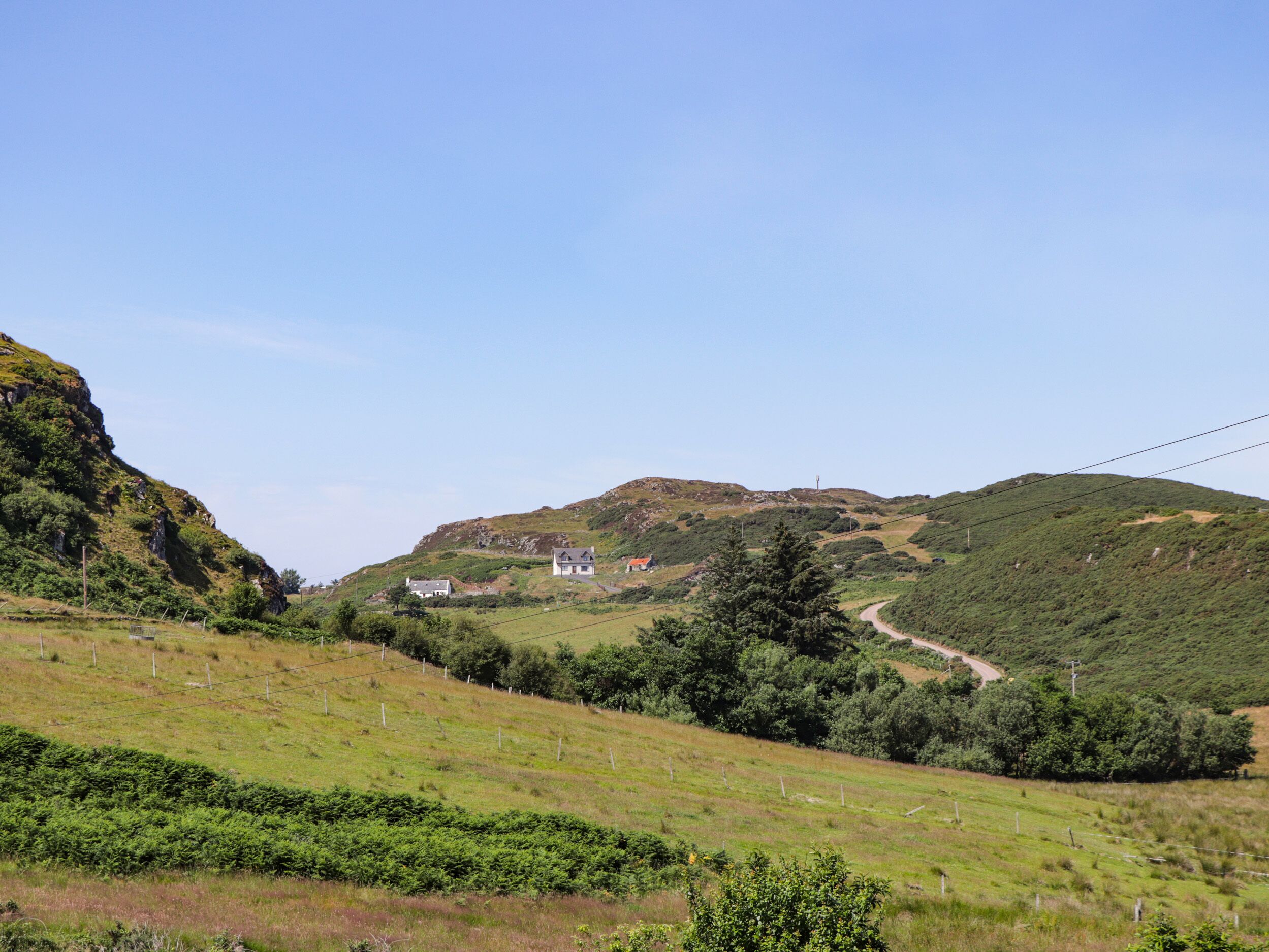 A rural landscape with rolling hills, a winding road, and a few houses.