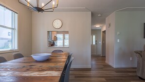 A dining area with a wooden table, chairs, a bowl, a clock, and a kitchen in the background.