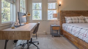 A bedroom with a wooden desk, computer, chair, and a bed with a checkered bedspread.