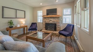 A living room with a stone fireplace, two blue chairs, a glass coffee table, and a sofa.