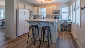 A modern kitchen with white cabinets, a central island with stools, a microwave, and a refrigerator.