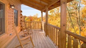 A wooden cabin with a covered porch, wooden chairs, and a view of autumn foliage. - 3 bed/3 bath luxury cabin with it's own private heated salt water pool! (Sevierville)