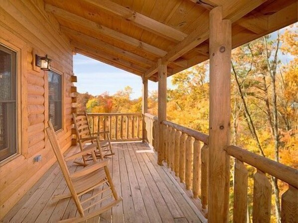A wooden cabin with a covered porch, wooden chairs, and a view of autumn foliage. - 3 bed/3 bath luxury cabin with it's own private heated salt water pool! (Sevierville)