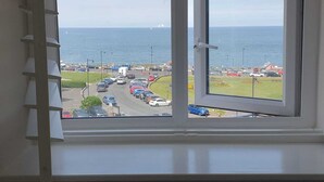 A room with a window overlooking a parking lot and the sea.