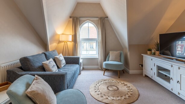 A cozy loft bedroom with a large window, a sofa, a chair, a TV, and a cabinet.
