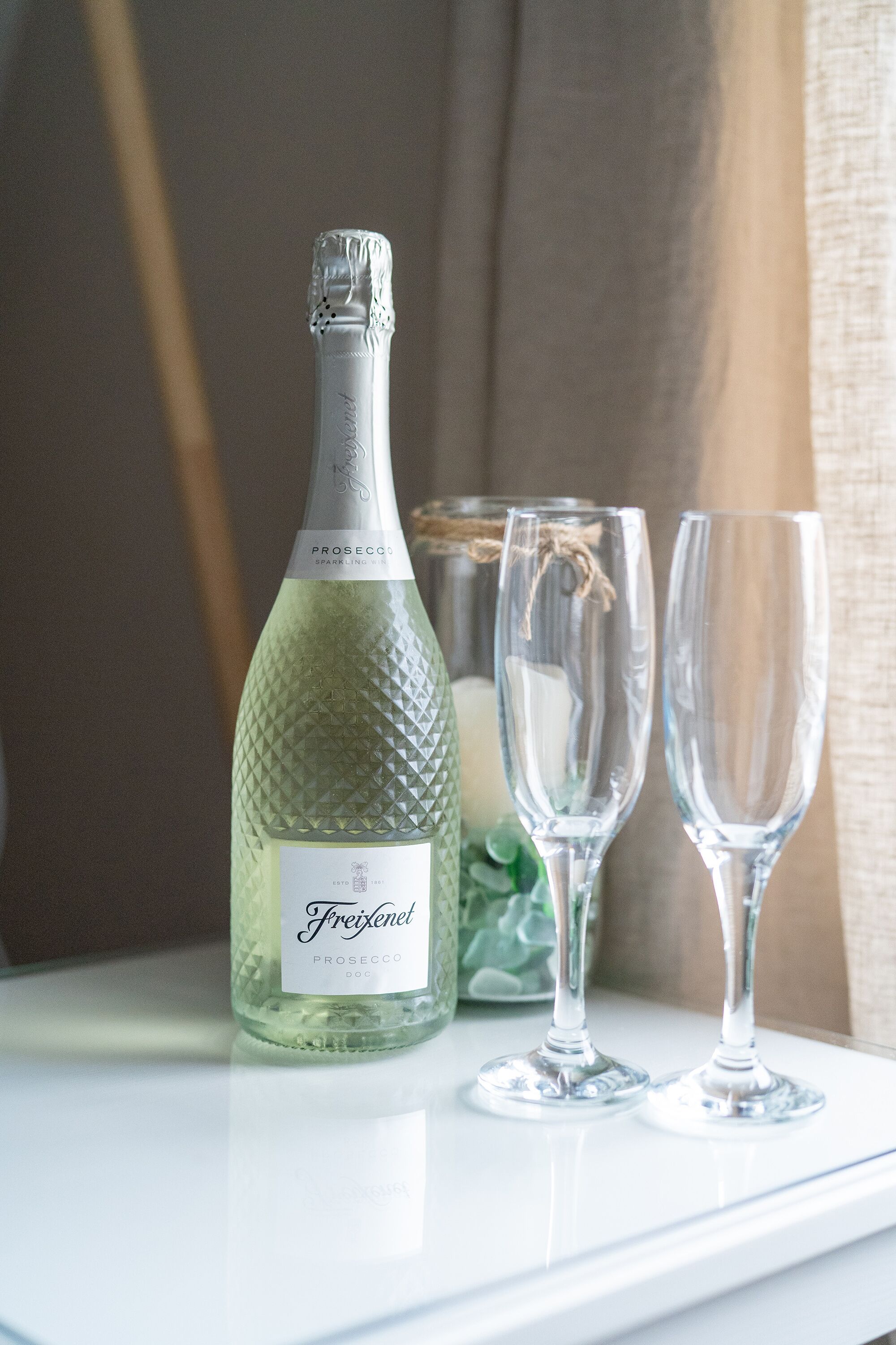 Een fles Freixenet Prosecco en twee lege wijnglazen op een witte ondergrond.