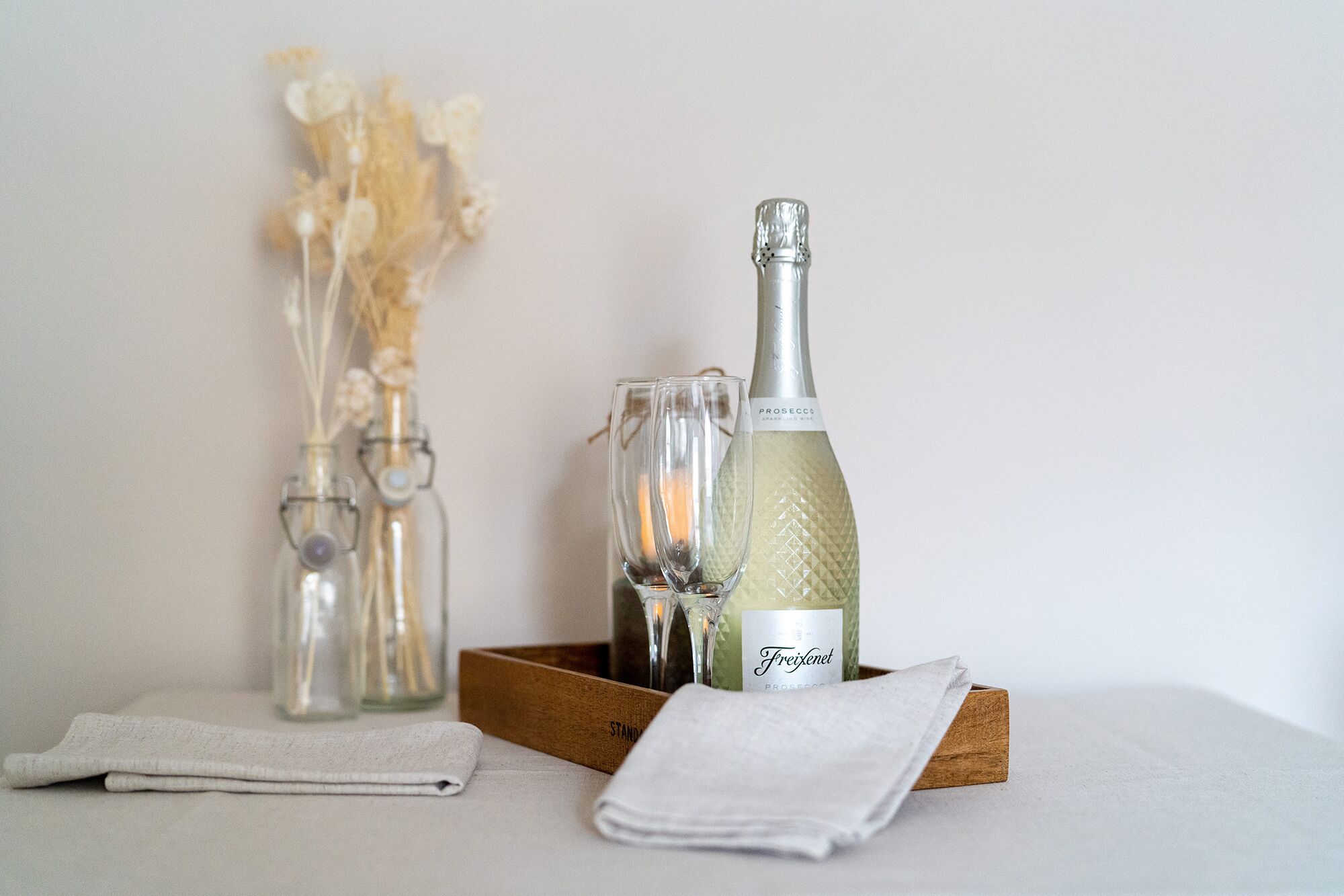 A bottle of Freixenet champagne, two glasses, and a wooden tray on a table with a white cloth.