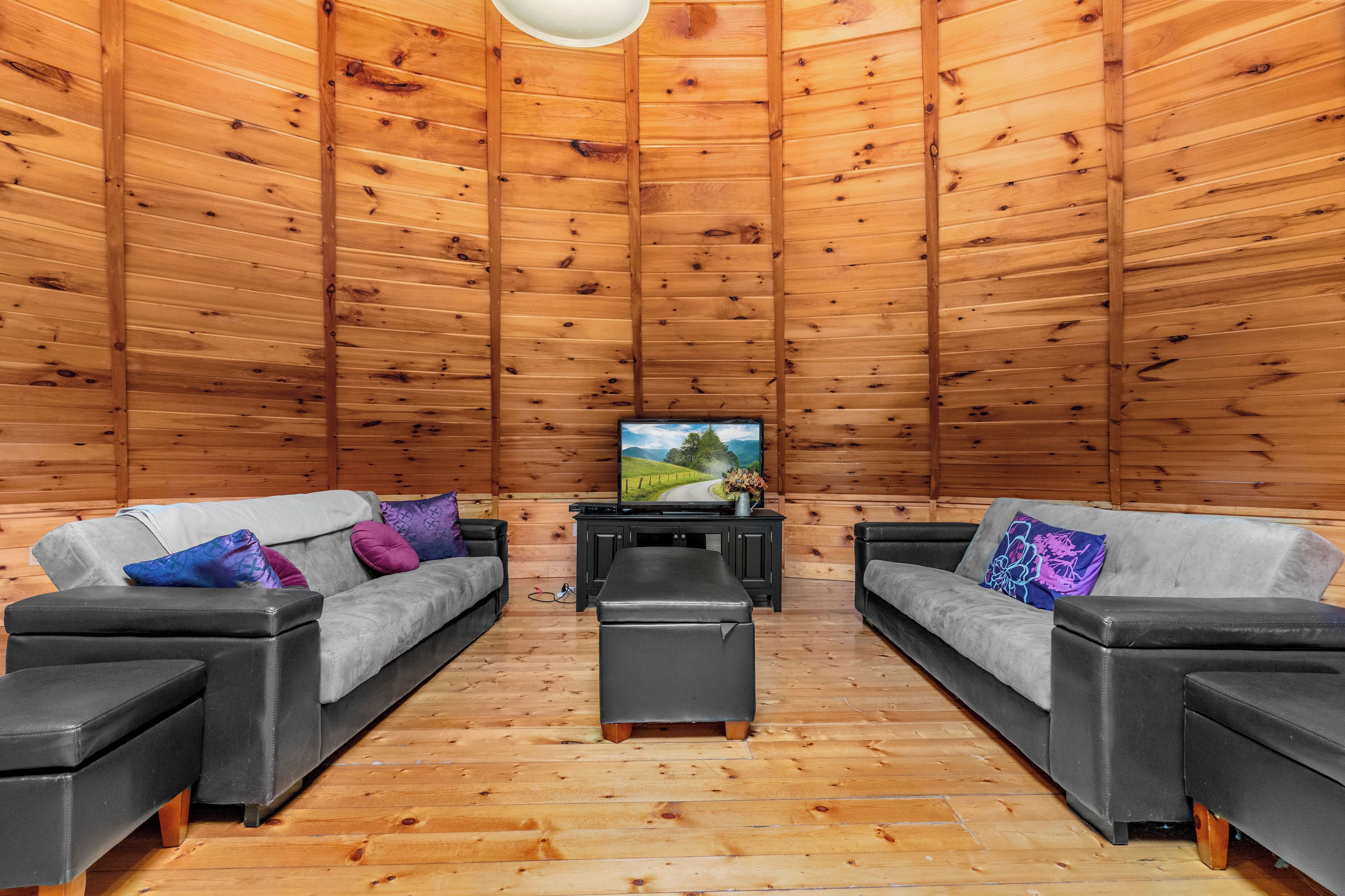 A cozy wooden cabin interior with two sofas and a bench, a television, and a wooden ceiling.