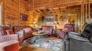 Interior de una cabaña de troncos con decoración de madera, un sofá, un sillón reclinable y una mesa de centro.