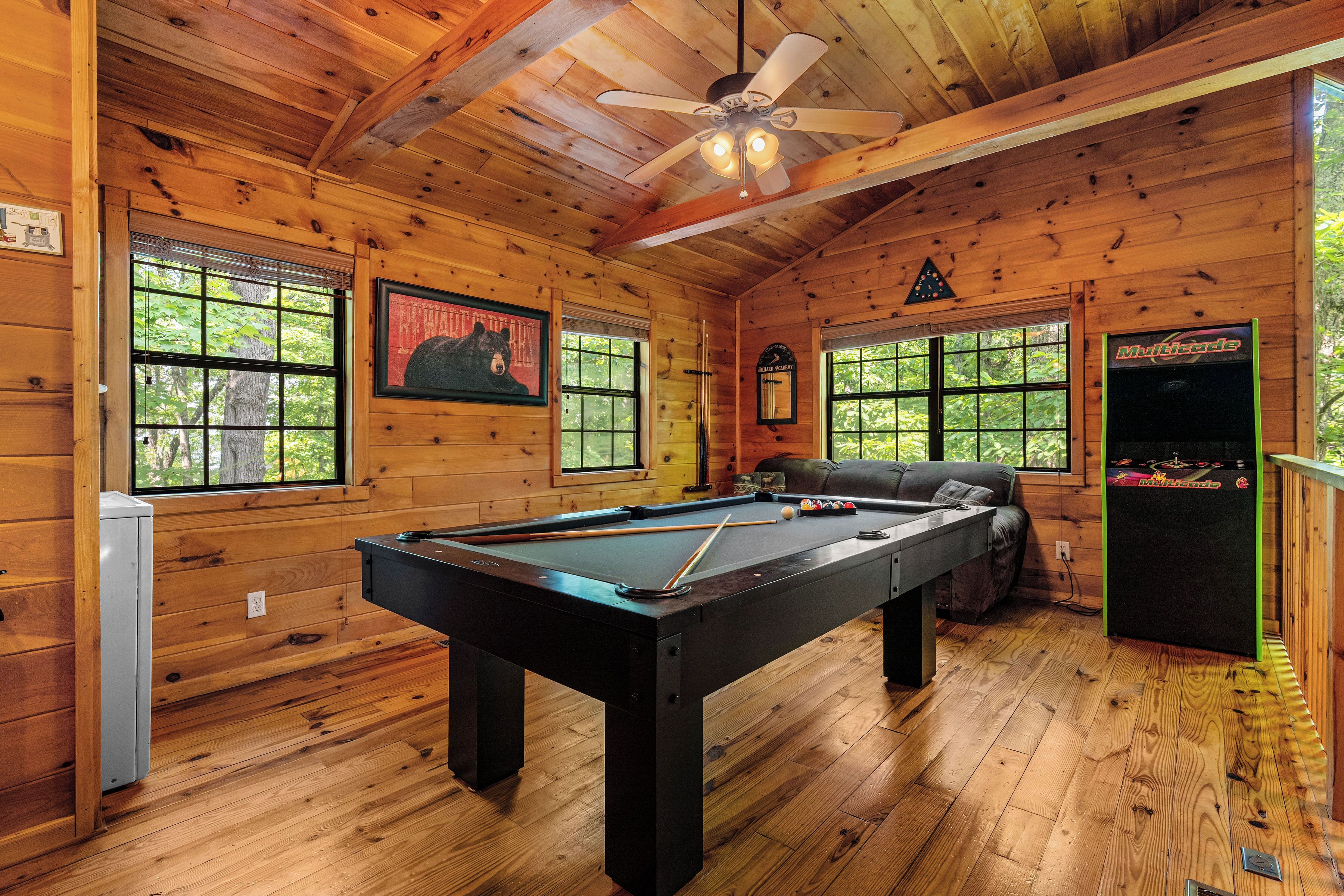 A wooden room with a pool table, a ceiling fan, and a billiards table.