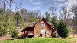 A log cabin with a porch, surrounded by trees and a grassy area. - Romantic Smoky Mountain Retreat with Hot Tub & Pool Table (Sevierville)