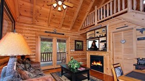 A cozy cabin interior with a fireplace, wooden walls, a dining area, and a ceiling fan. - Romantic Smoky Mountain Retreat with Hot Tub & Pool Table (Sevierville)