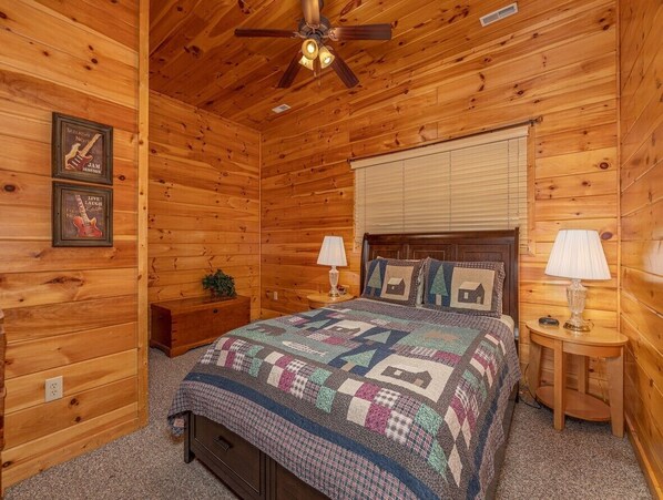 A wooden cabin bedroom with a bed, two nightstands, a ceiling fan, and a quilt. - A Must See! 5 Bedroom/4 Bathroom Cabin (Sevierville)