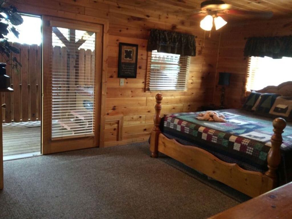Une chambre située dans une cabane en bois, avec un lit, une fenêtre équipée de stores et une porte donnant sur une terrasse extérieure.