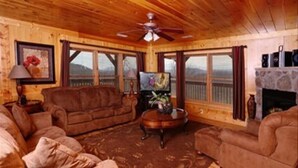 Una sala de estar acogedora con paredes y techo de madera, un conjunto de sofá marrón, una mesa de centro, un televisor y una chimenea.