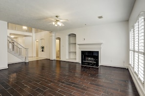 A spacious living area with dark wooden flooring, a fireplace, a ceiling fan, and a staircase leading to an upper level. - Cinco Ranch Katy Texas, upscale living (Katy)