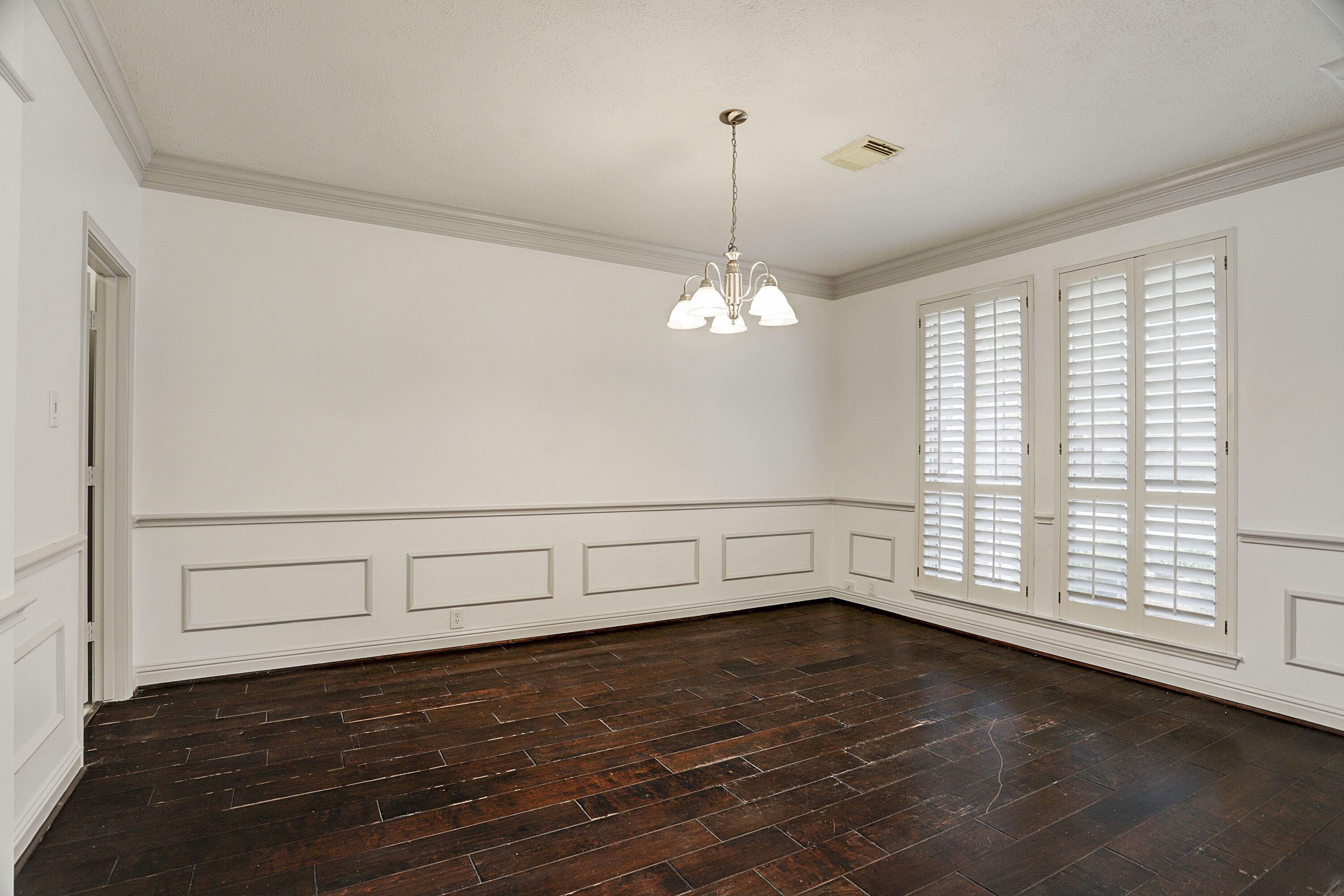 Una habitación con suelo de madera oscura, paredes blancas y una lámpara en el techo.