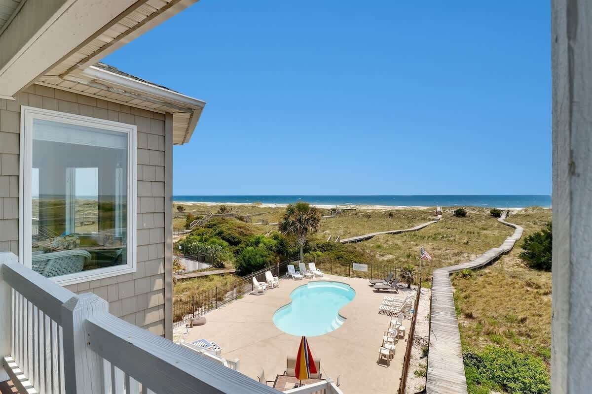 A pool with lounge chairs, a wooden deck, and a view of the beach and ocean.