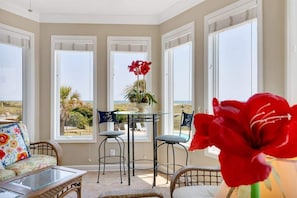 Habitación soleada con vista al mar, una mesa con sillas y un sofá de mimbre.
