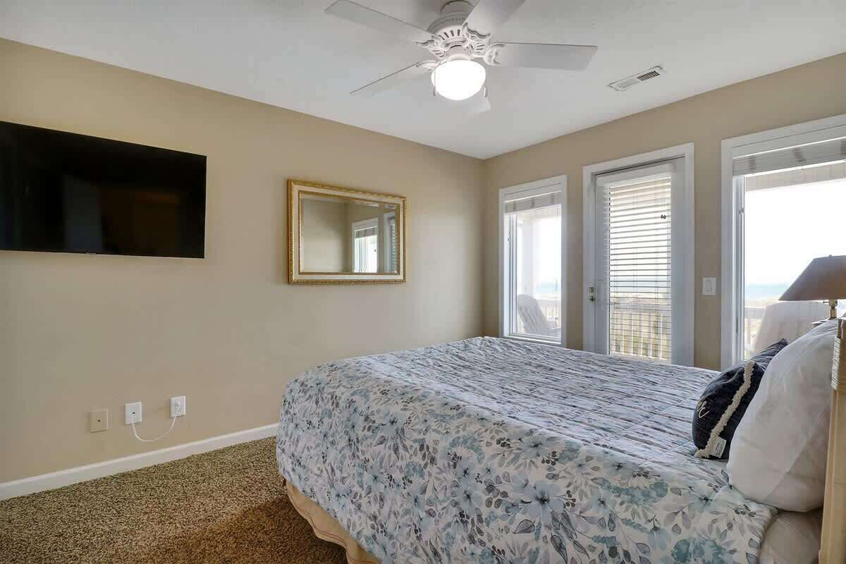 Une chambre à coucher avec un lit, un ventilateur de plafond, un téléviseur fixé au mur et une porte donnant sur l’extérieur.