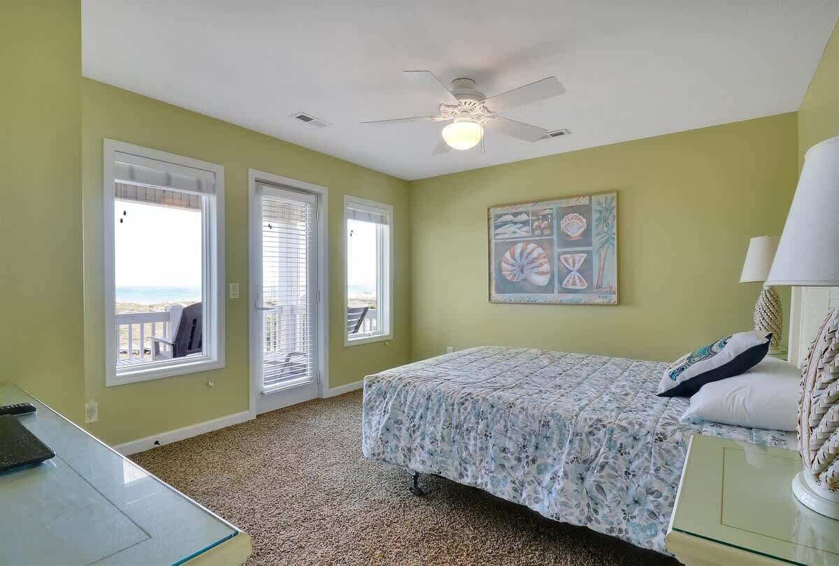 A bedroom with a bed, a ceiling fan, a window, and a painting on the wall.