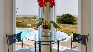 Ein Eckzimmer mit Glastisch und zwei Stühlen, einer Vase mit roten Blumen und Blick auf den Strand.