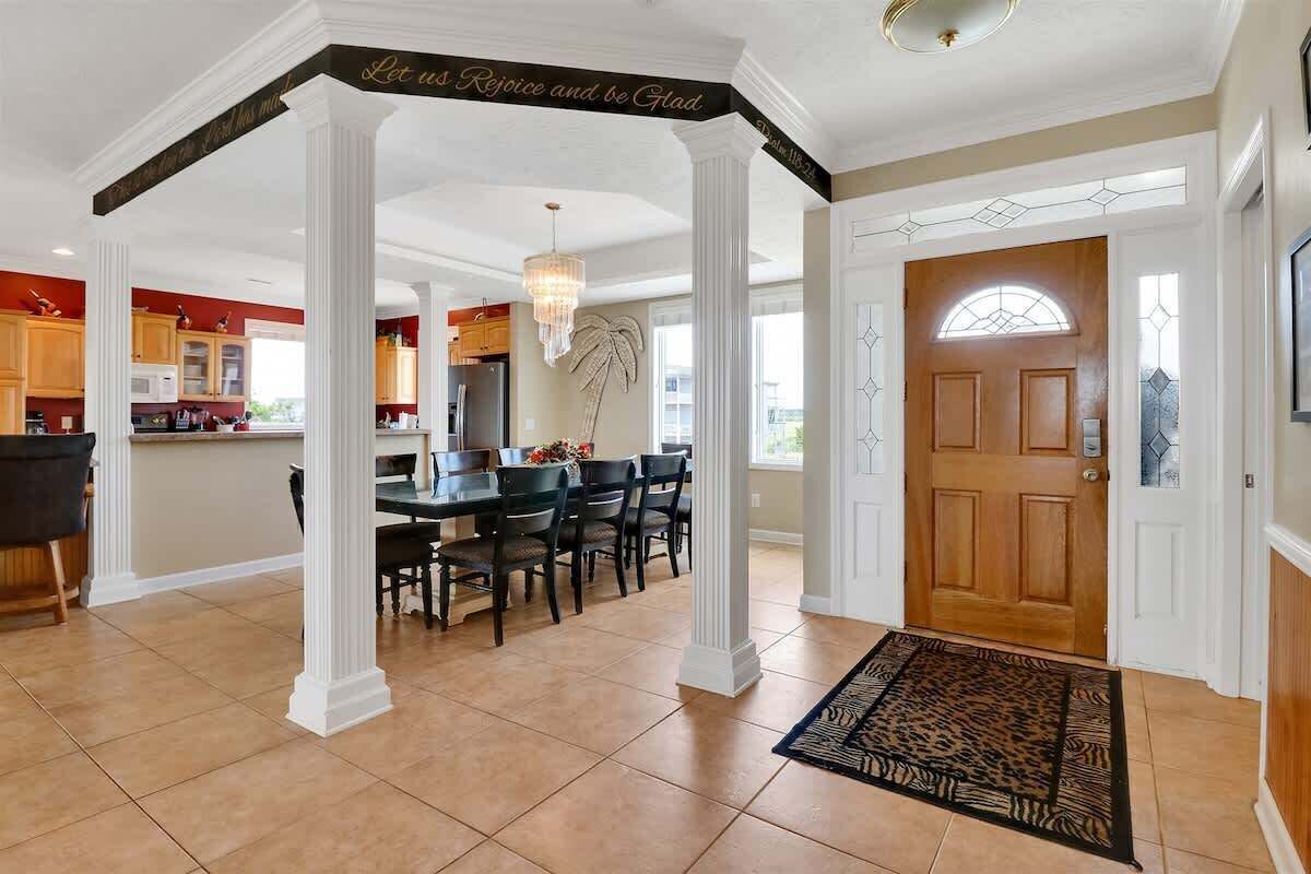 A spacious kitchen with modern appliances, a dining area with a chandelier, and a foyer with a wooden door and a decorative rug.