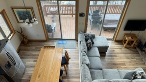 Ein großzügiger Wohnbereich mit einem Holzessttisch, einem grauen Sofa und einer großen Schiebeglasdoor zur Terrasse.