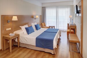 Habitación de hotel con una cama grande, dos mesitas de noche, un escritorio, una silla y un televisor montado en la pared.
