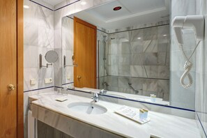 A modern bathroom with a marble sink, a glass shower enclosure, and a hairdryer mounted on the wall. - Hotel Girasol (Sant Llorenc des Cardassar)