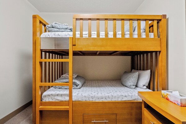 A bunk bed with a wooden frame, a lower bed with patterned bedding, and a bedside table with a tissue box. - Cozy Rockies Stay - Ground Floor w/ Hot Tub, BBQ (Dead Man's Flats)