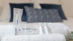 Un juego de artículos de aseo personal ordenado sobre una toalla blanca, que incluye un tubo etiquetado "Voyager" y una bolsa de plástico transparente con la misma marca visible.