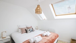 Een moderne slaapkamer met een groot bed, witte beddengoed, een rode plaid en een unieke geweven hanglamp.