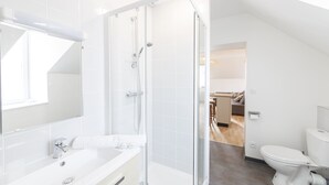 Een moderne badkamer met een douchecabine van glas, een wit wastafelmeubel en een toilet.