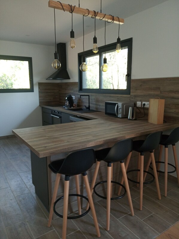 Una cocina moderna con una isla de madera, taburetes negros y luces colgantes.