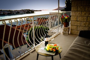 Un balcon avec une table dressée pour deux personnes, agrémenté d’un panier de fruits et de verres à vin.