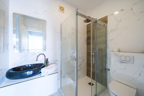 Een moderne badkamer met een douchecabine van glas, een marmeren wastafel en een toilet.