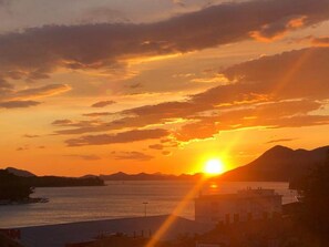 Een zonsondergang boven het water met bergen op de achtergrond.