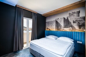 Een hotelkamer met een groot bed, uitzicht op een kasteel door een raam en een balkon.