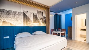 A hotel room with a large bed, a desk with a chair, a small table with a chair, and a bathroom visible through an open door. - Apartments Tayra - Comfort Studio with Balcony (BR3) (Dubrovnik)